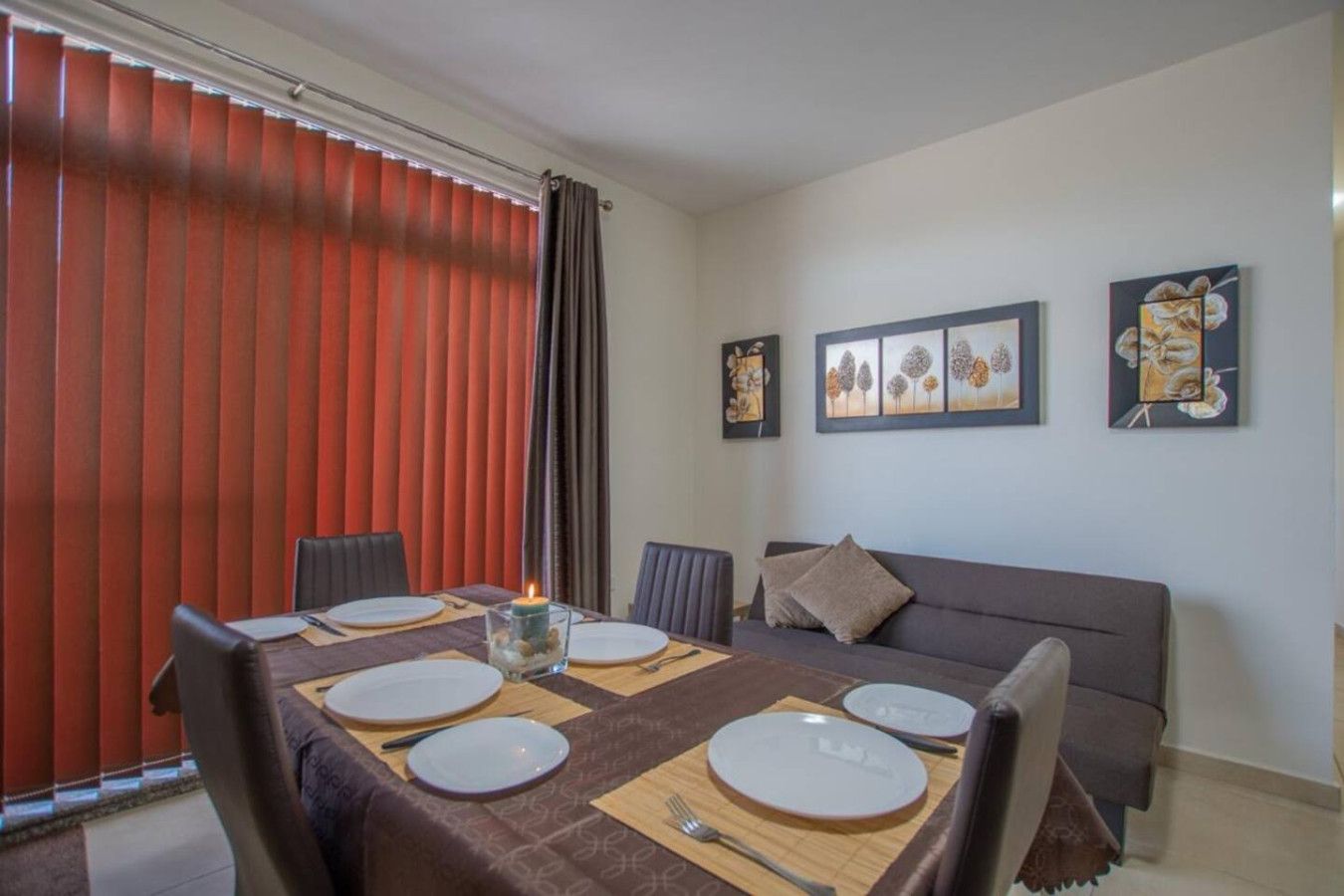 A dining area with a table set for four, a sofa, and artwork on the wall.