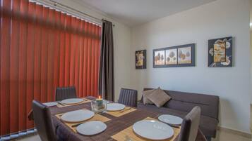 A dining area with a table set for four, a sofa, and artwork on the wall.