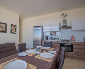A modern kitchen with a dining area, equipped with a refrigerator, oven, and a clock on the wall.