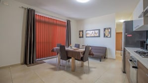 A dining area with a table and chairs, a sofa, and a kitchen area with a stove. - The Terrace apartment (Xgħajra)