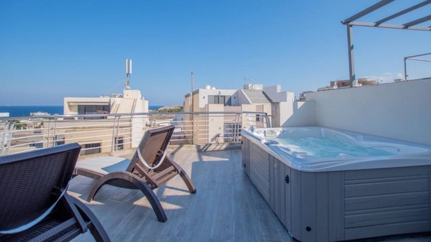 A rooftop terrace with a hot tub, seating area, and a view of the sea and buildings. - The Terrace apartment (Xgħajra)