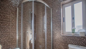 A bathroom with a glass-enclosed shower, a sink, and a window with a plant. - The Terrace apartment (Xgħajra)