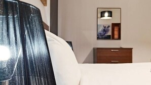 Una habitación de hotel con cama, mesita de noche, lámpara y un cuadro en la pared.