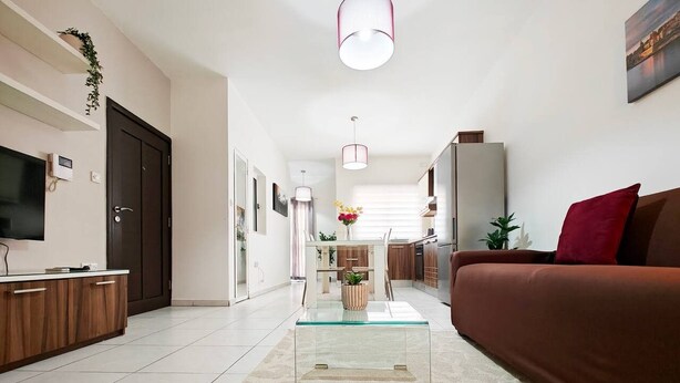 Una sala de estar moderna con una mesa de centro de vidrio, un sofá y un televisor sobre un mueble de madera.