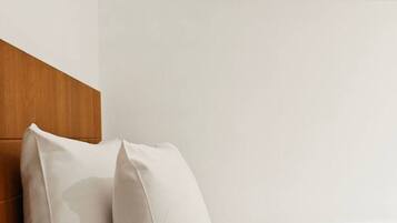 A bed with white linens and two pillows, a wooden headboard, and a wooden shelf above the bed.