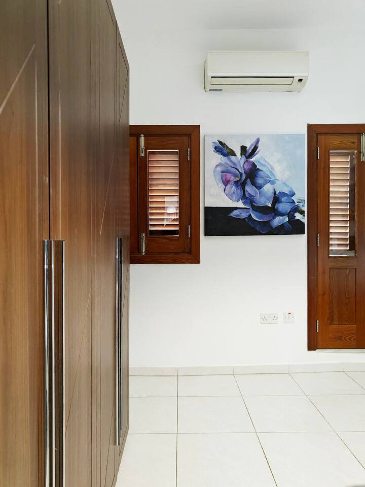 Ein Zimmer mit einem großen Holzschrank, zwei Holztürrahmen und einer Wandleuchte sowie einem Blumenbild.