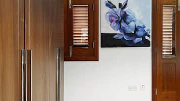 A room with a large wooden wardrobe, two doors with wooden frames, a wall-mounted air conditioner, and a floral painting.