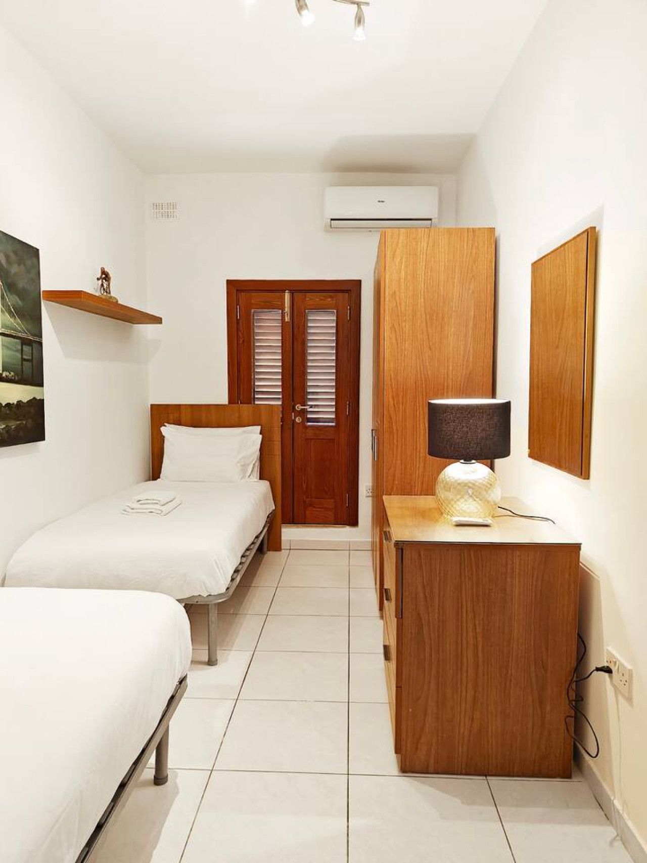 Een slaapkamer met een bed, een dressoir, een spiegel en een deur met luiken.