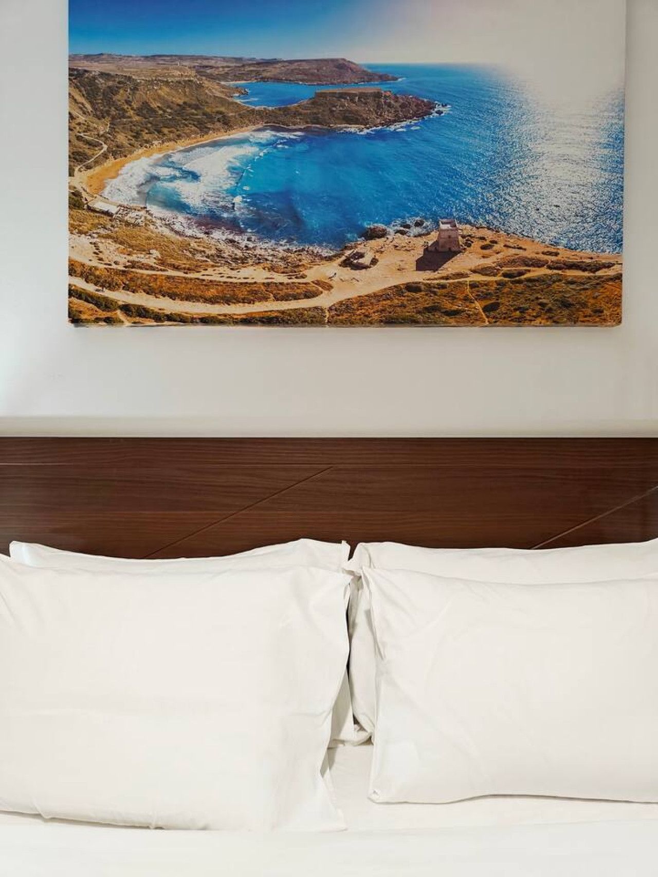 Ein Schlafzimmer mit einem Bett, weißen Kissen und einem Gemälde einer Küstenlandschaft.