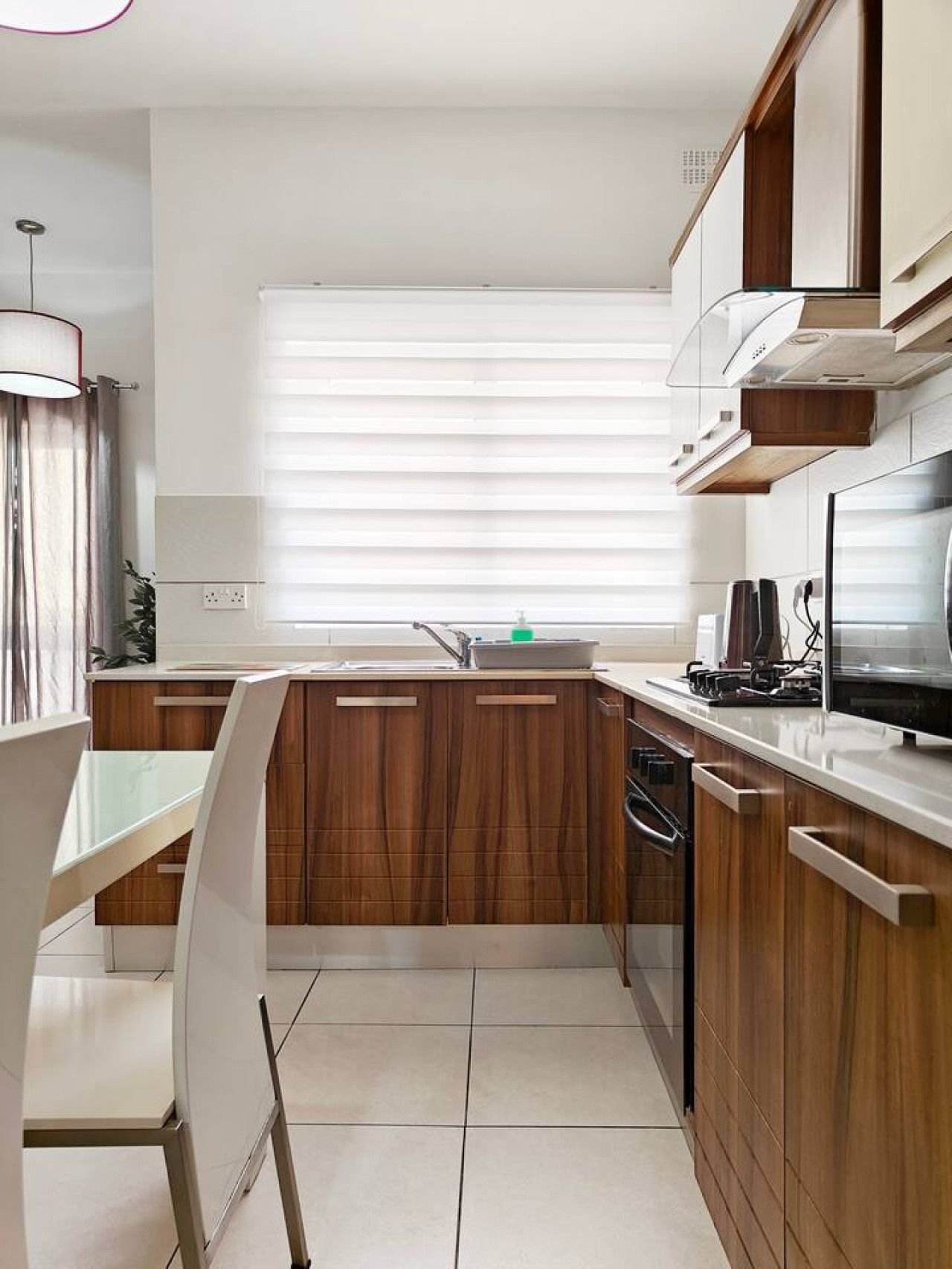 A modern kitchen with wooden cabinets, a white countertop, and a window with blinds.