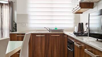 A modern kitchen with wooden cabinets, a white countertop, and a window with blinds.