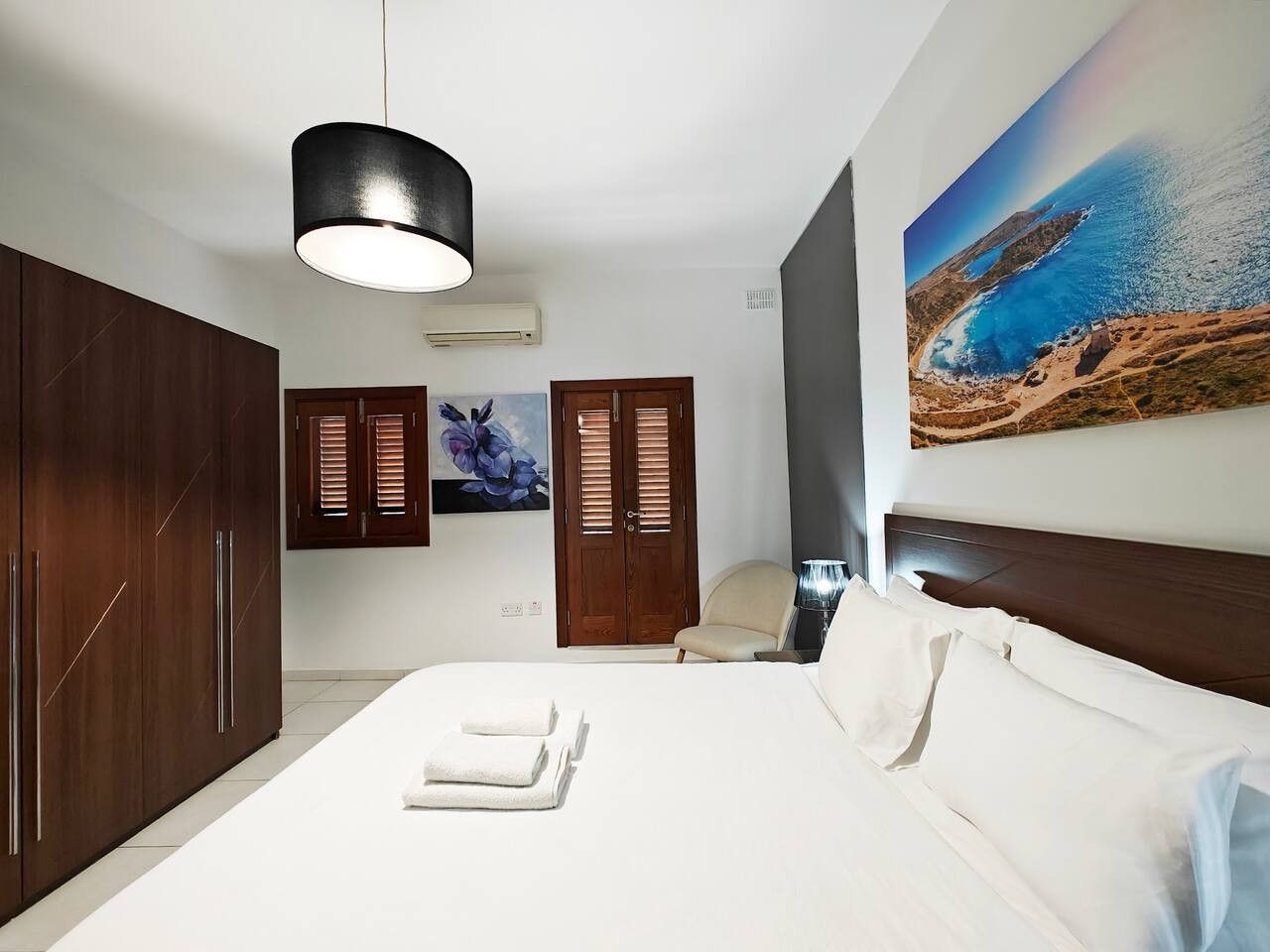 Ein Schlafzimmer mit einem großen Bett, einem Holzschrank und einem Gemälde einer K üstenlandschaft.