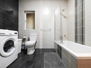 Ein modernes Badezimmer mit Waschmaschine, Toilette und Badewanne.