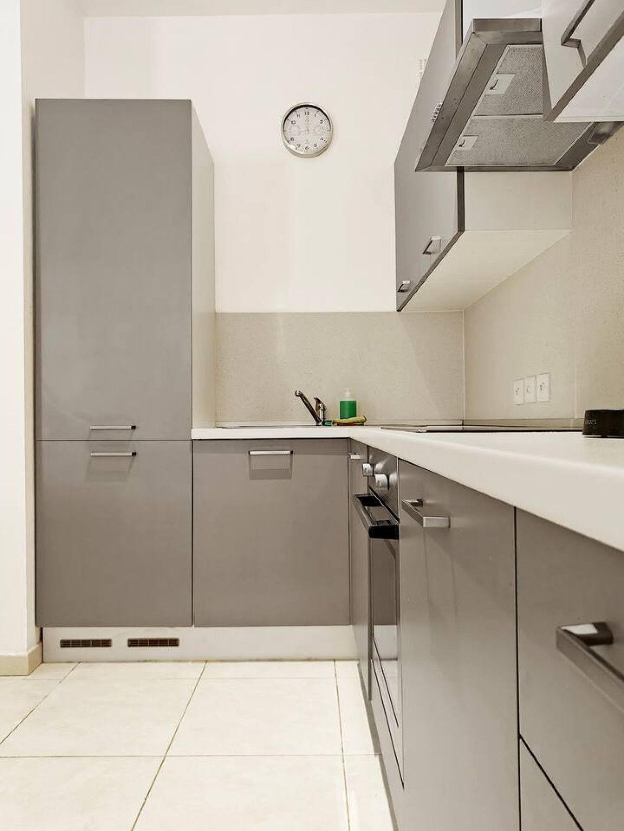 A modern kitchen with grey cabinets, a white countertop, and a clock on the wall.