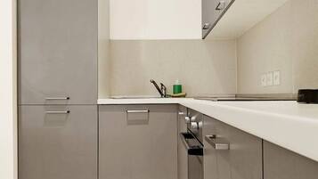 A modern kitchen with grey cabinets, a white countertop, and a clock on the wall.