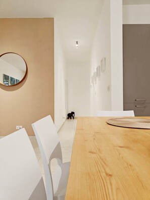 Ein modernes Interieur mit einem Holzesstisch, weißen Stühlen, einem runden Spiegel und einem Flur, der zu einer Küchenecke führt.