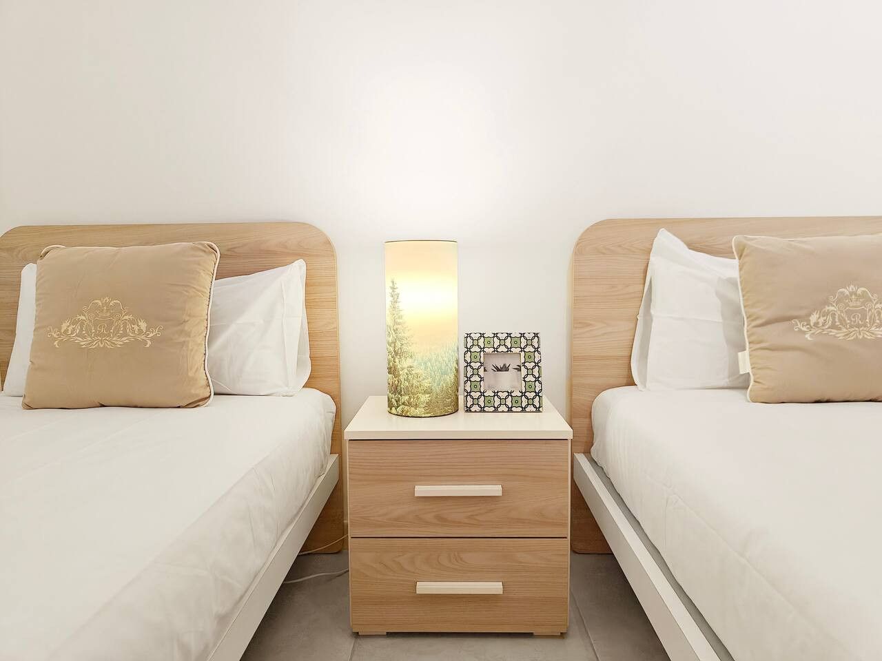 A hotel room with two beds, a bedside table with drawers, and a lamp.