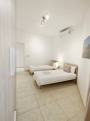 A hotel room with two beds, a ceiling light, an air conditioning unit, and a painting on the wall.