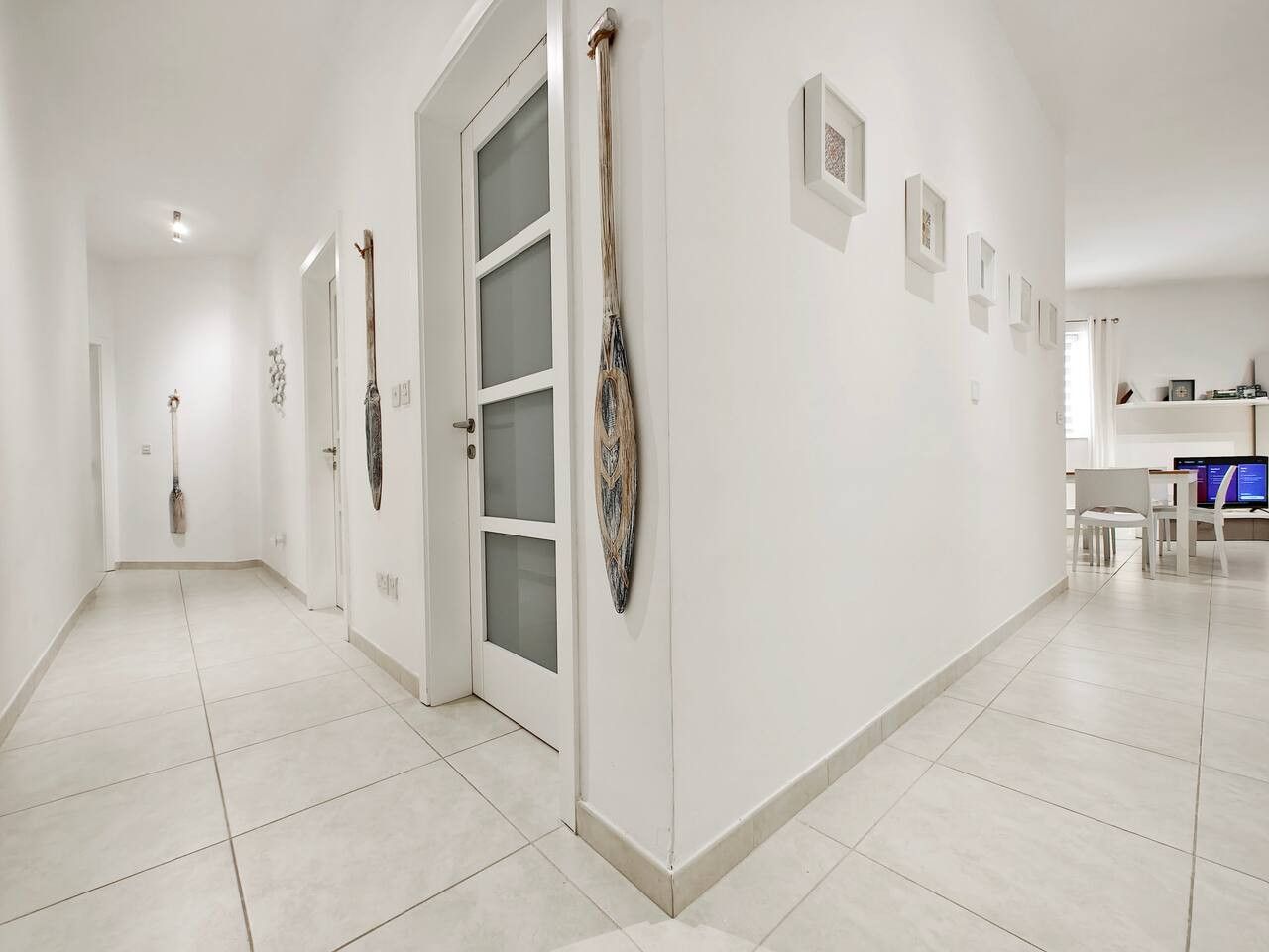 A hallway with white walls, a door with frosted glass panels, and a series of framed pictures on the wall.