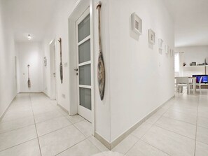 A hallway with white walls, a door with frosted glass panels, and a series of framed pictures on the wall.