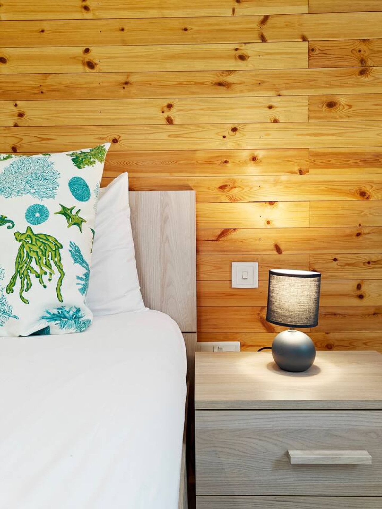 A neatly made bed with a white comforter and a pillow with a marine life print.