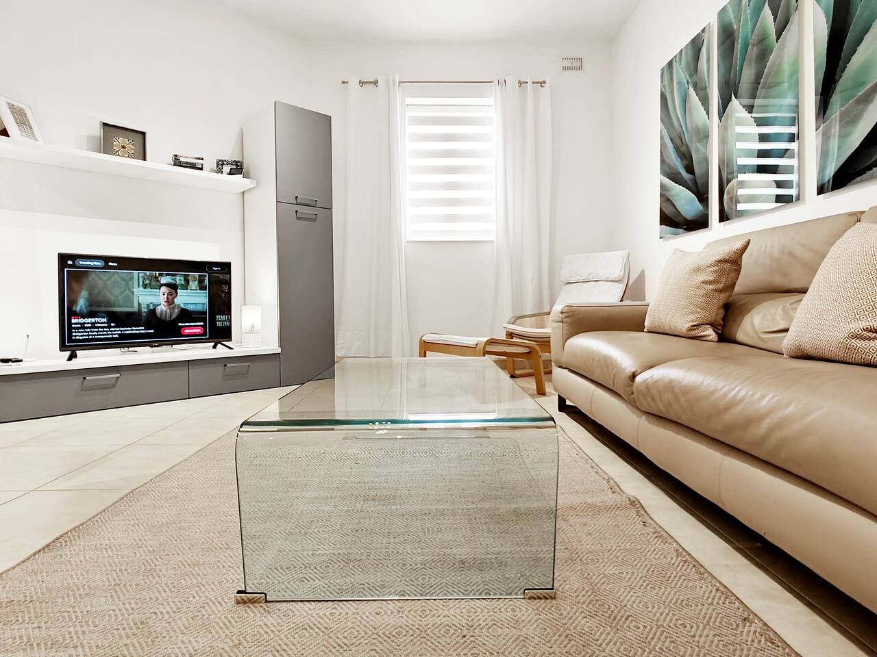 A modern living room with a glass coffee table, a beige sofa, and a flat-screen TV on a stand.