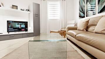 A modern living room with a glass coffee table, a beige sofa, and a flat-screen TV on a stand.