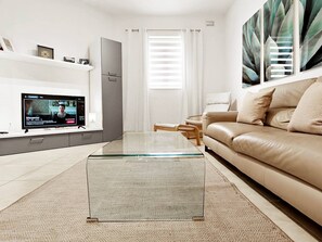 Un saló modern amb una taula de centre de vidre, un sofà beix i una televisió de pantalla plana sobre un suport.