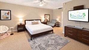 A bedroom with a bed, bedside tables, a chair, a dresser, a television, and a ceiling fan. - Ocean Club 1005 Enjoy Panoramic Views of the Gulf! (Biloxi)