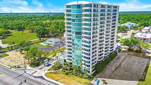 A high-rise hotel with multiple balconies, a swimming pool, and a parking area. - Ocean Club 1005 Enjoy Panoramic Views of the Gulf! (Biloxi)