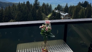 A balcony with a table, a vase with flowers, and a mountain view.
