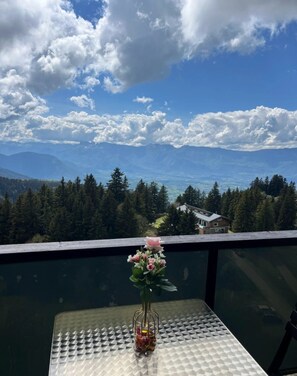 Un balcó amb una taula, un vas amb flors i vista a la muntanya.