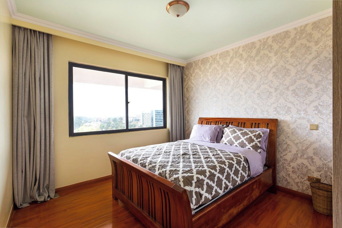 A bedroom with a wooden bed, a large window, and patterned wallpaper.