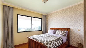 A bedroom with a wooden bed, a large window, and patterned wallpaper. - Crestpark Penthouse Spectacular Views (Nairobi)