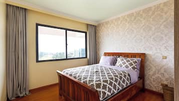 A bedroom with a wooden bed, a large window, and patterned wallpaper.