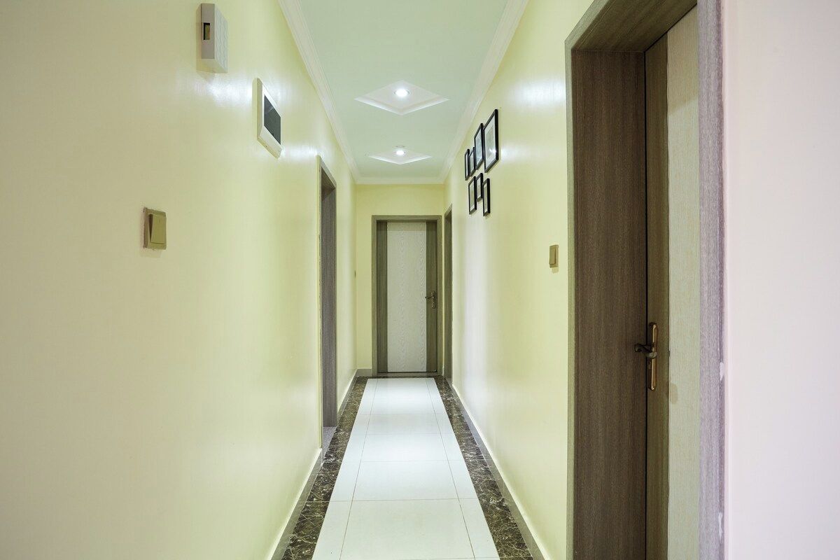 A hallway with a door at the end, a light switch, and a wall-mounted light fixture.