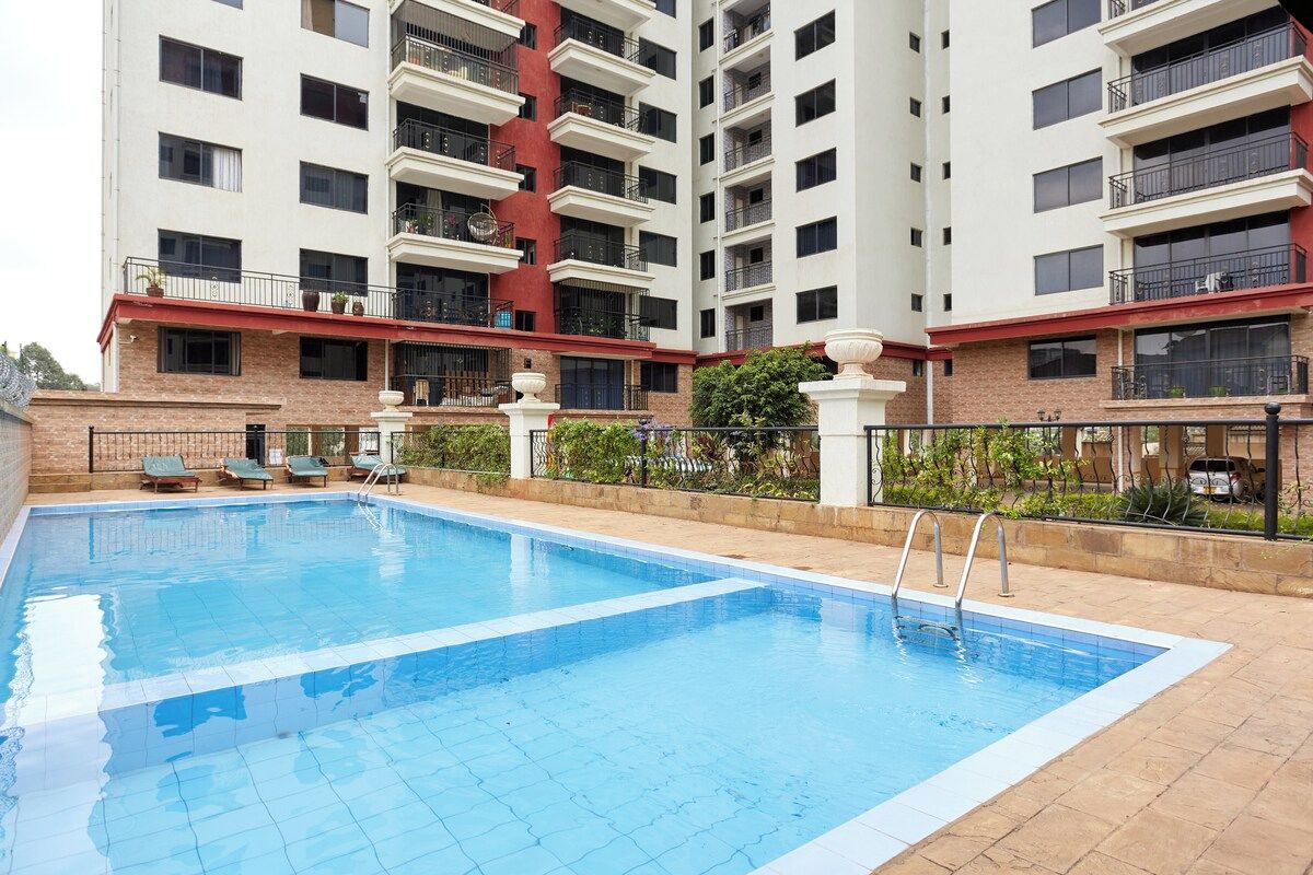 A swimming pool with lounge chairs, surrounded by a multi-story building with balconies.