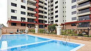 A swimming pool with lounge chairs, surrounded by a multi-story building with balconies. - Crestpark Penthouse Spectacular Views (Nairobi)