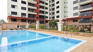 A swimming pool with lounge chairs, surrounded by a multi-story building with balconies.