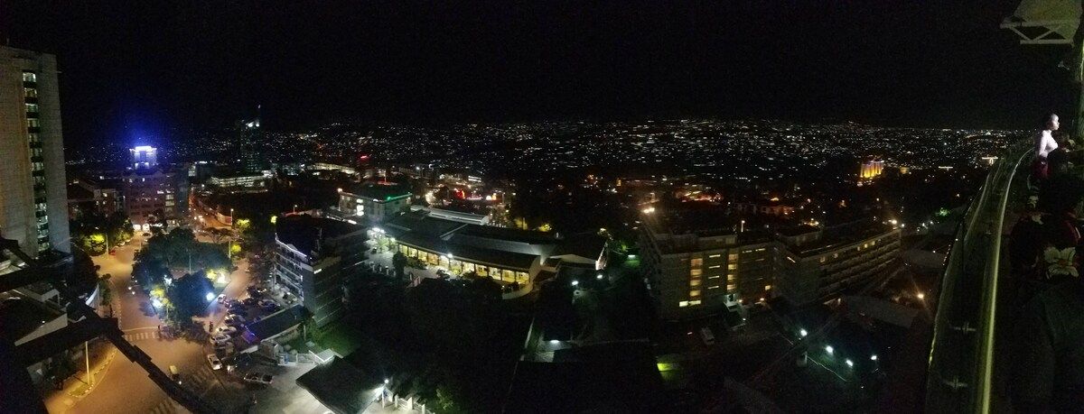 A nighttime cityscape with illuminated buildings and a central plaza.