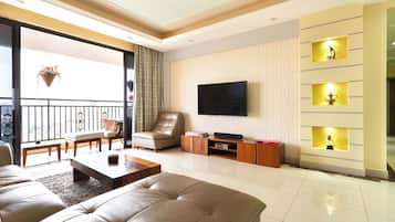 A modern living room with a large sofa, a flat-screen TV, and a balcony with a view.