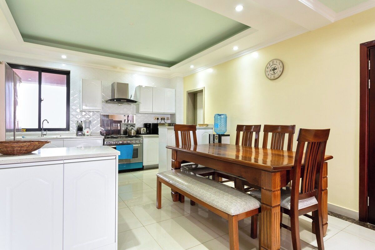 A modern kitchen with white cabinets, a wooden dining table, and a bench.