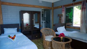 Ett hotellrum med en säng, två fåtöljer i rotting, ett litet bord, en garderob och ett fönster med gardiner.