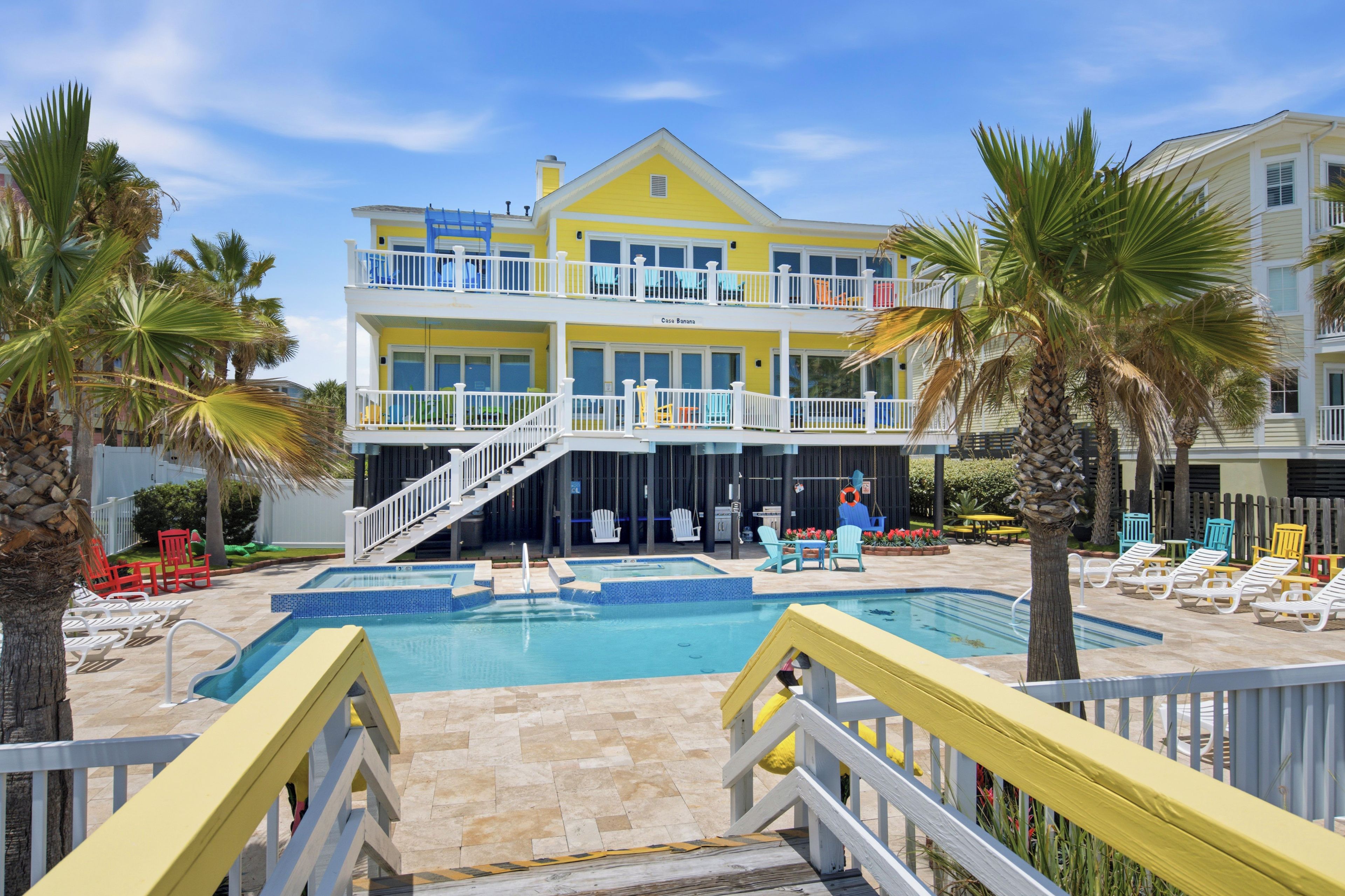 Un bâtiment à deux étages doté d’une piscine, d’un espace extérieur aménagé et de palmiers.
