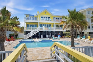 A two-story building with a pool, outdoor seating, and palm trees. - Oceanfront home with multiple pools and hot tub (Isle of Palms)
