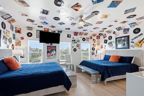 Une chambre avec deux lits, un ventilateur de plafond et des murs décorés de divers affiches et de pochettes de disques vinyles.
