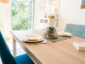 A dining area with a wooden table set for two, a blue chair, and a view of greenery outside. - Holiday Apartment 2 "hooge" (Tating)