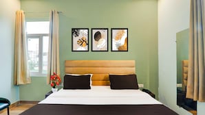 A bedroom with a bed, two pillows, a nightstand, a vase with flowers, and three framed artworks on the wall. - Collection O Malhaur Railway Station (Lucknow)