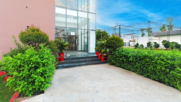 A modern building with a glass facade, a concrete entrance, and a well-maintained garden with red planters. - Collection O Malhaur Railway Station (Lucknow)