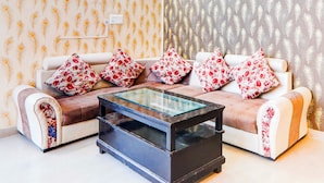 A living room with a sofa set, a glass coffee table, and patterned wallpaper. - Collection O Malhaur Railway Station (Lucknow)
